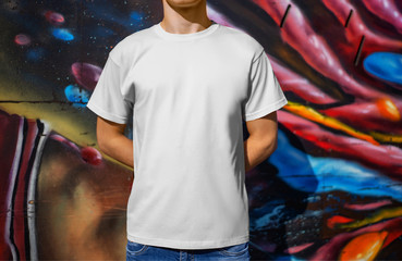 Mockup white t-shirt on a young guy, against the background of a wall with graffiti, front view.