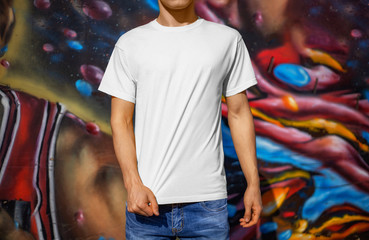 Mockup of a white T-shirt on a young guy against the background of a colorful wall, outdoors, front...