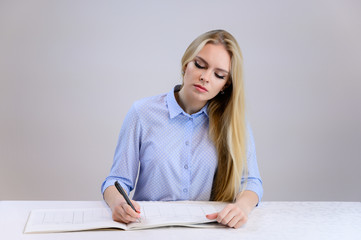 Concept cute model student secretary works sitting at a table. Close-up portrait of a beautiful blonde girl with excellent makeup with long smooth hair on a white background in a blue shirt.