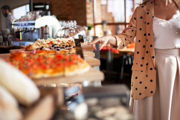 Matured middle aged woman dressed style fasnion clothes chooses the pastry bakery on showcase table in cafe.