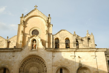 Fototapeta na wymiar Detail of the church of San Giovanni Battista in Matera. Facade in tufa stone. Bells and statue of the saint and portal in Arabic style.