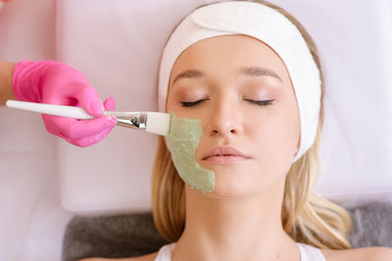 Cosmetologist applying mask on face of  woman in spa salon
