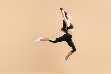 Fototapeta na wymiar A young attractive brunette woman with a ponytail jumps, dances, flies, stretches out, against a peach background.