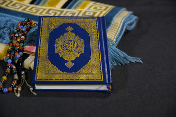Closuep of Muslims Holy book Quran with a Colorful Tasbeeh Paternoster and Prayer rug Janamaz on black background 