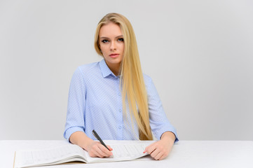 Concept cute model student secretary works sitting at a table. Close-up portrait of a beautiful blonde girl with excellent makeup with long smooth hair on a white background in a blue shirt.