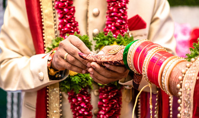 Fototapeta na wymiar Engagement Ring ceremony- Indian Hindu male putting ring on bride's decorated finger. Couple is well attired as per traditional Indian Hindu wedding. Groom wearing Jodhpuri suit and floral garland.