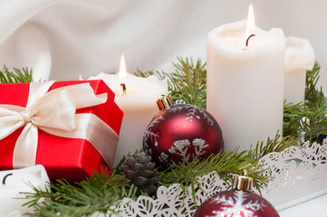 Christmas or New Year card. White burning candles on a light background. Red balls and boxes with gifts. Stand on fir branches