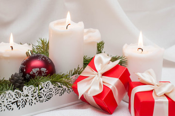 Christmas or New Year card. White burning candles on a light background. Red balls and boxes with gifts. Stand on fir branches