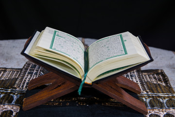 Muslims Islamic Holy Book Quran Majid with Quran wooden stand and Janamaz Prayer Rug and black background 