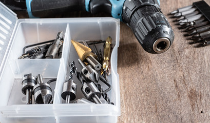 Variety of different types of bit drill in transparent organizer box on old wooden background.