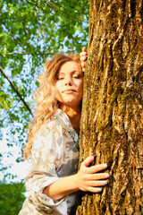 Beautirul girl with curly blonde hair near a tree in the park with sunny weather