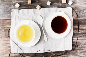 Two cups of black and green tea with cane and white sugar cubes on wooden rustic table. Top view.