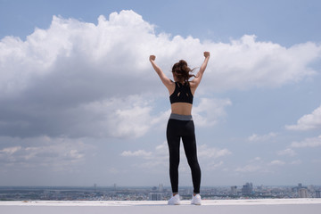 Obraz premium Rear view of beautiful woman in stylish sportswear standing on the rooftop. After the workout