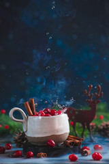 Obraz na płótnie Canvas Cranberry winter drink with water drops, cinnamon, steam, and a wooden decorative deer.