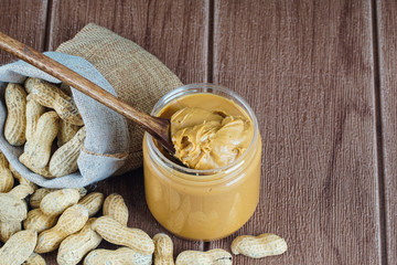 Peanut butter in a glass jar with a full sack of ground nut and on the the wooden table. selective focus