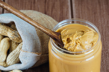 Peanut butter in a glass jar with a full sack of ground nut and on the the wooden table. selective focus