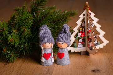 Christmas decoration of wooden table: 2 toy figures (girl, boy) with twig of decorative christmas tree & wooden christmas toy in form of christmas tree on background. Close-up, selective focus. Christ