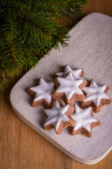 Fototapeta na wymiar Christmas cookies (cinnamon stars, Zimtsterne in German) on wooden plate on wooden table with twig of decorative christmas tree. Selective focus, close-up. Christmas wallpaper.