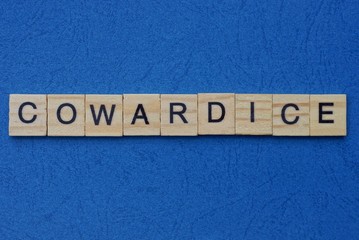 word cowardice made from brown wooden letters lies on a blue table 