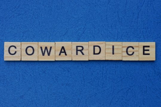 word cowardice made from brown wooden letters lies on a blue table 