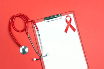 Empty medical folder with red ribbon as symbol of aids awareness and stethoscope on red background.