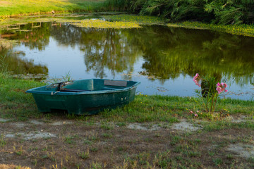 A small lake with a green rowing boat laying on the grass
