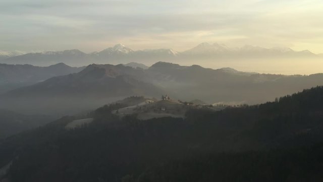 Aerial view flying over foggy landscape in Slovenia viewing the Alps in the distance.
