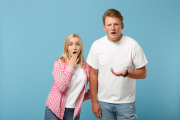 Naklejka premium Young fun couple two friends guy girl in white pink empty blank design t-shirts posing isolated on pastel blue background studio portrait. People lifestyle concept. Mock up copy space. Looking upset.