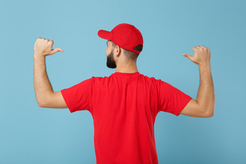 Back view delivery man in red uniform workwear isolated on blue background studio portrait. Professional male employee in cap t-shirt print working courier dealer. Service concept. Mock up copy space.