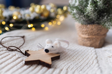 A white toy mouse or a rat with a wooden star and christmas tree and lights background. Year of the...