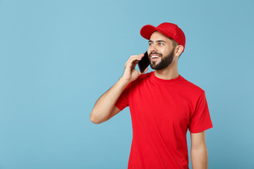 Delivery man in red uniform workwear hold cellphone isolated on blue background, studio portrait. Professional male employee in cap t-shirt working courier dealer. Service concept. Mock up copy space.