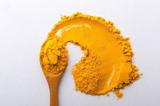 Closeup of wooden spoon and turmeric on the white table.Top view of turmeric condiment
