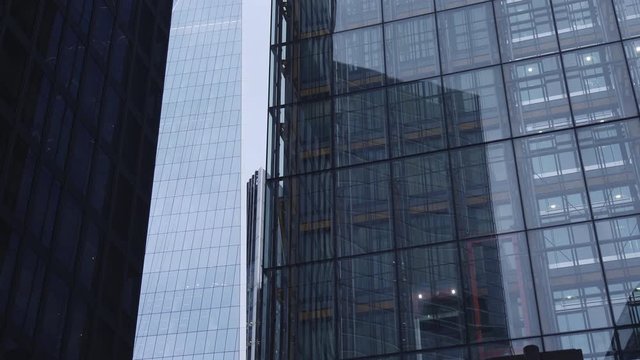 A Skyscraper With Shiny Reflective Windows And With An Elevator By The Side Overlooking The Surrounding Buildings In The City Of London On A Cloudy Day - Tilt Up Shot