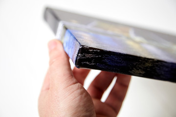 Canvas print. Hand holds a photo with gallery wrap method of canvas stretching on stretcher bar. Sample of stretched color photograph printed on canvas, lateral side, closeup.