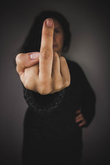 Woman with dark sweater showing middle finger. Black background.