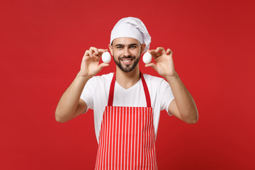 Smiling young bearded male chef cook or baker man in striped apron white t-shirt toque chefs hat isolated on red background in studio. Cooking food concept. Mock up copy space. Holding eggs in hands.