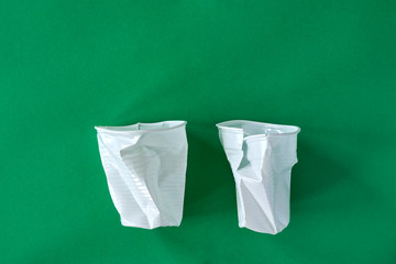Two smashed white plastic coffee cups on a green background with copy space. Zero waste, plastic free, stop pollution, ecological concept.