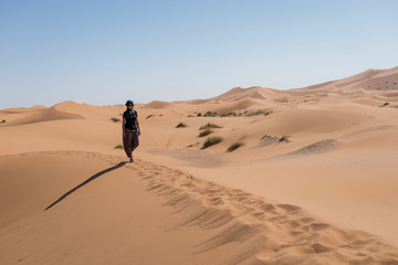 Fototapeta na wymiar Woman walking in the dunes in the Moroccan Sahara desert.