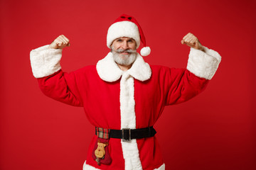 Fototapeta na wymiar Strong elderly gray-haired mustache bearded Santa man in Christmas hat posing isolated on red background. Happy New Year 2020 celebration holiday concept. Mock up copy space. Showing biceps, muscles.