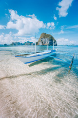 El Nido, Palawan, Philippines. Banca boat on sandy beach in shallow crystal clear water on island hopping trip. Amazing Pinagbuyutan island in background. Beautiful landscape scenery