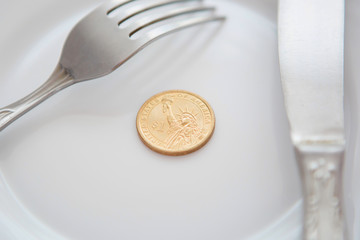One dollar coin on a white plate next to fork and knife