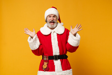 Fototapeta na wymiar Excited elderly gray-haired mustache bearded Santa man in Christmas hat posing isolated on yellow wall background. Happy New Year 2020 celebration holiday concept. Mock up copy space. Spreading hands.