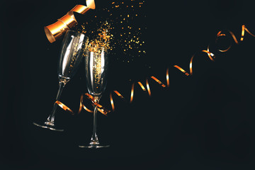 Two champagne glasses with golden sparkles over black background. Happy new year.