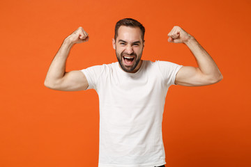 Strong crazy young man in casual white t-shirt posing isolated on orange background, studio portrait. People sincere emotions lifestyle concept. Mock up copy space. Showing biceps, muscles screaming.