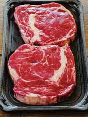 Two raw uncooked premium fresh rib eye steaks on a plastic tray, Top quailty product from supermarket. On a wooden table.