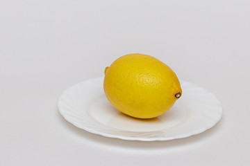 Bright yellow lemon on a white plate, on a white paper background. A component of the vegetarian menu. 