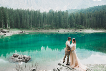 Wedding couple on the nature is hugging each other near a beautiful lake in the mountains.. Beautiful model girl in white dress. Man in suit