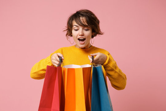 Excited young brunette woman girl in yellow sweater posing isolated on pink wall background in studio. People lifestyle concept. Mock up copy space. Holding package bag with purchases after shopping.