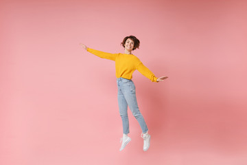 Fototapeta na wymiar Smiling young brunette woman girl in yellow sweater posing isolated on pastel pink background in studio. People lifestyle concept. Mock up copy space. Having fun spreading hands rising hands, jumping.