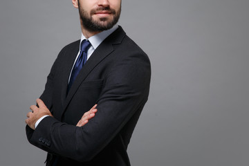 Obraz na płótnie Canvas Cropped image of young bearded business man in classic black suit shirt tie posing isolated on grey background. Achievement career wealth business concept. Mock up copy space. Holding hands crossed.